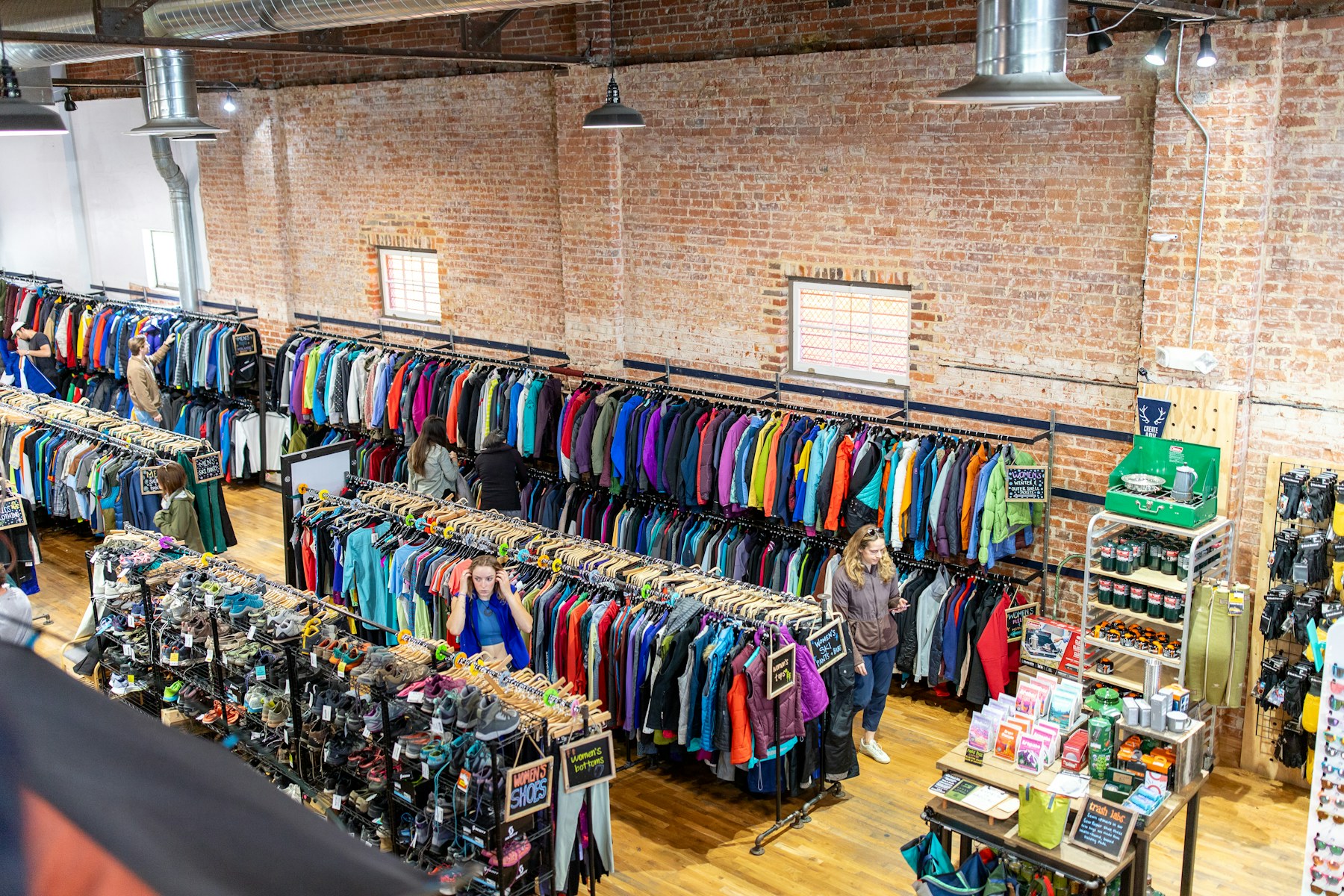A wide view of a sports apparel store interior, with rows of colourful jackets on hanging rails and a shoe display below, seen from a mezzanine.